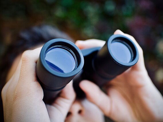 Person, die durch ein Fernglas nach oben schaut.