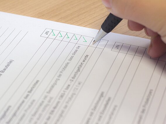Hand, die mit einem Kugelschreiber eine Checkliste ausfüllt.