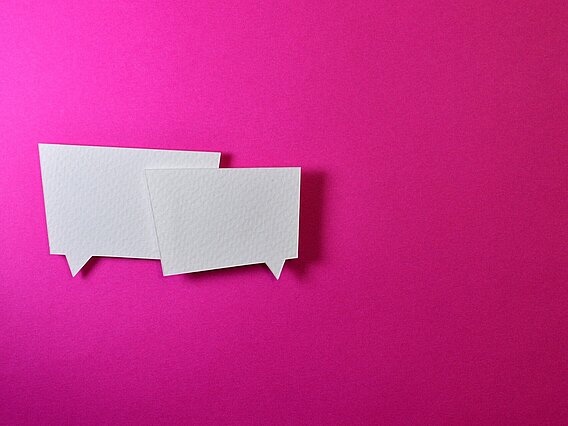 Zwei weiße Sprechblasen aus Papier auf pinkem Hintergrund