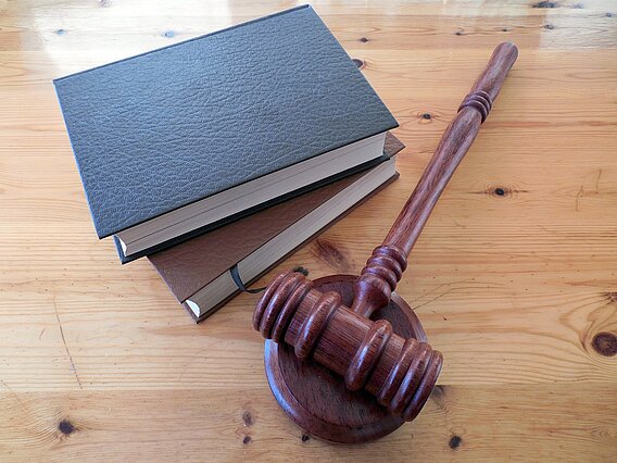Zwei Bücher mit dunklem Einband, daneben ein Richterhammer aus Holz