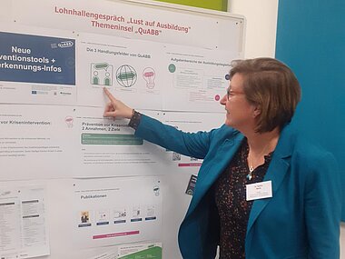 Sabine Beck von der QuABB-Koordinierungsstelle zeigt auf eine Stellwand zum Thema Prävention von Ausbildungsabbrüchen.
