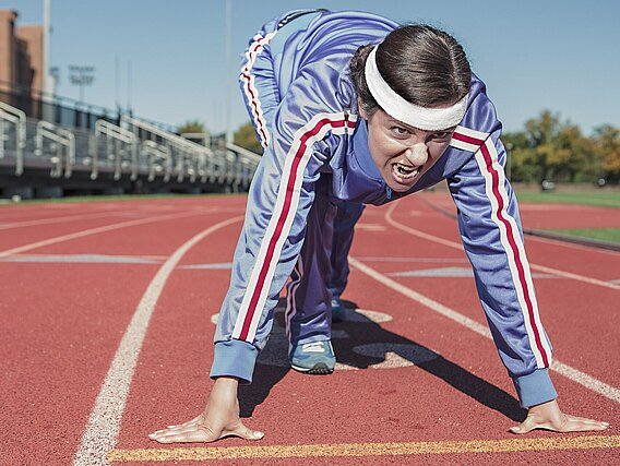 Junge Person in Sportkleidung auf einem Sportplatz in Startposition.