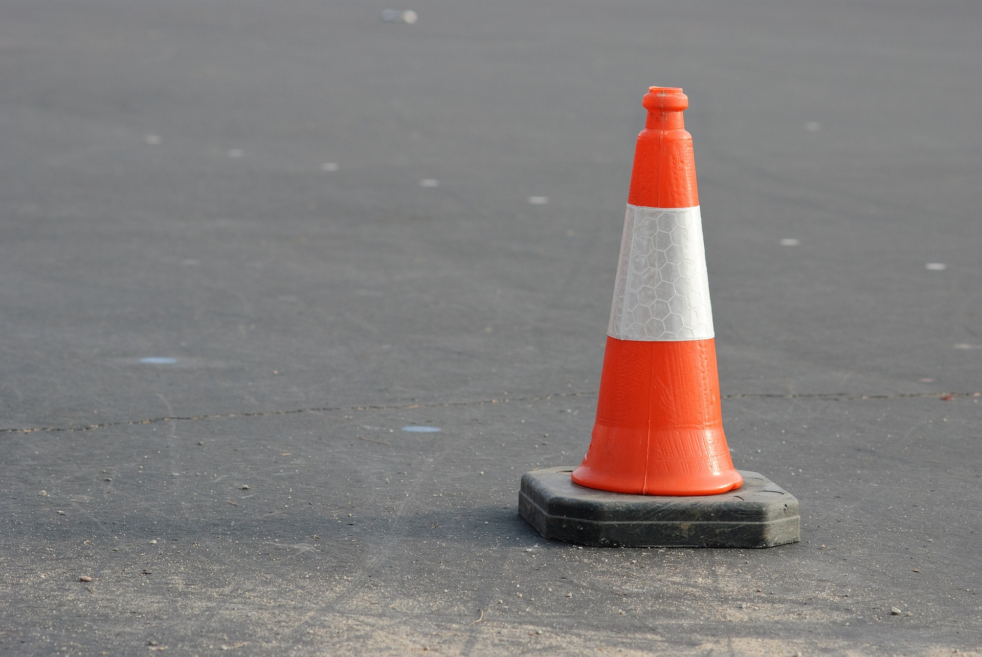 Orange-weiß gestreifter Warnkegel auf grauem Asphalt